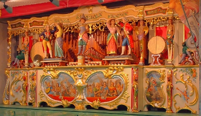 [Colorful figures in front of a long row of gold pipes (pipe organ is part of this). Lower portion are colorful ornate scenes.]